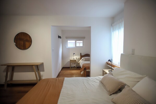 Un dormitorio con cama, mesitas de noche, un escritorio de madera, un radiador y una ventana con cortinas.
