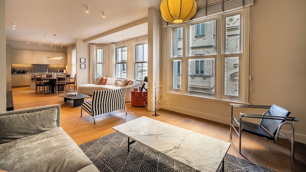 Un vaste espace de vie comprenant un canapé, une table basse, un fauteuil à rayures et une lampe moderne.