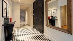 Un couloir doté d’un sol à carreaux noirs et blancs, d’une porte noire et d’œuvres d’art encadrées accrochées aux murs.