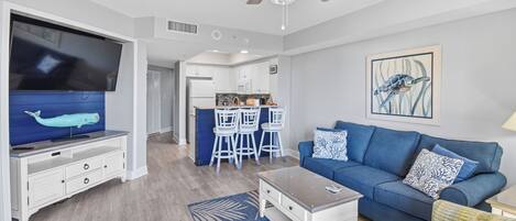 A modern living room with a blue sofa, white coffee table, and a flat-screen TV.