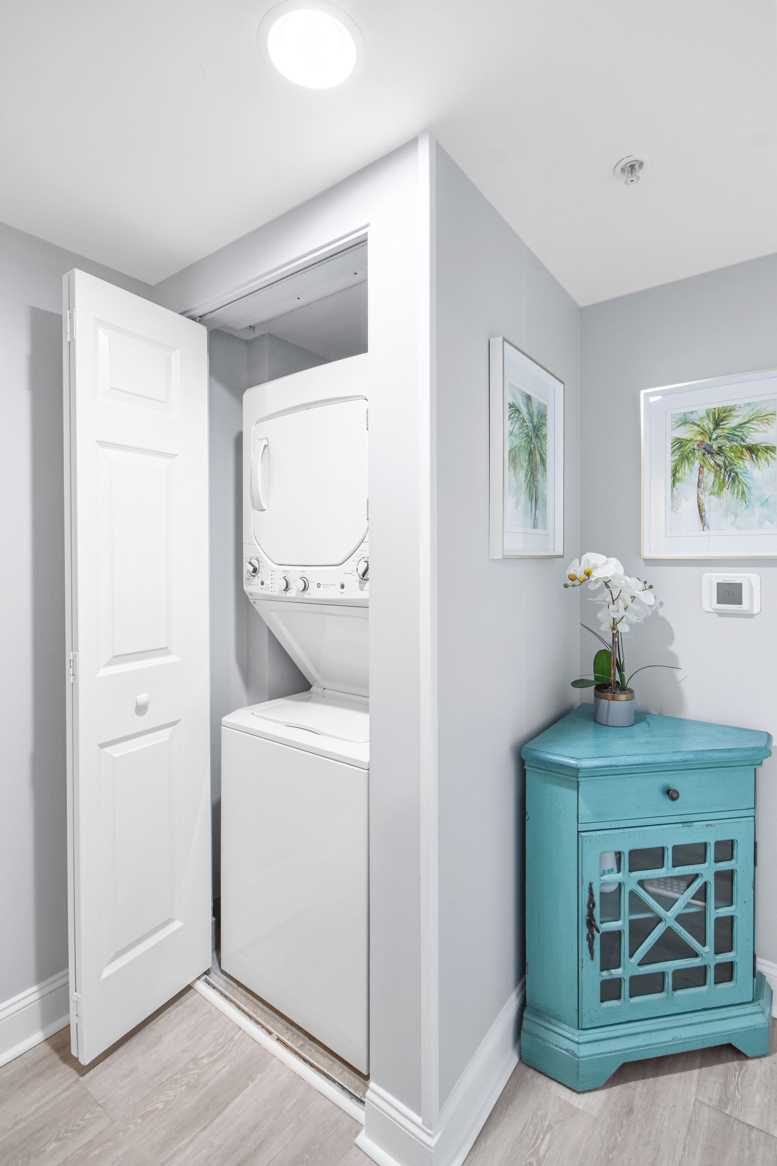 A laundry room with a white washer and dryer, a teal cabinet, and two framed pictures on the wall.