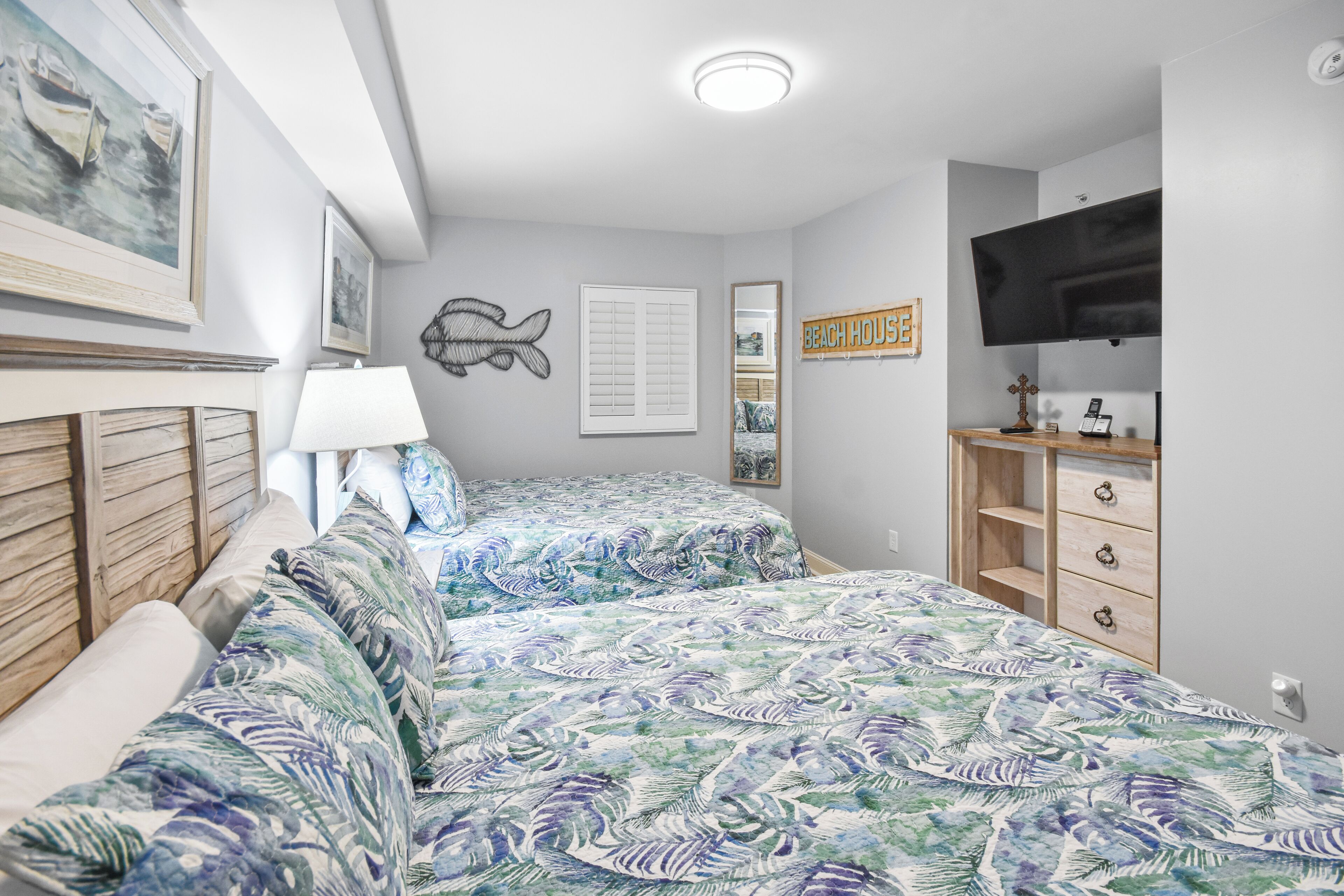 A bedroom with two beds, a TV, a dresser, and artwork on the walls.