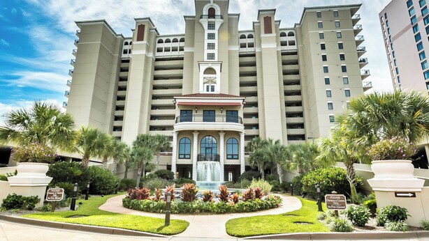 Suuri hotelli, jossa on keskeisellä paikalla sijaitseva suihkulähde, useita parvekkeita ja runsas viheralue.