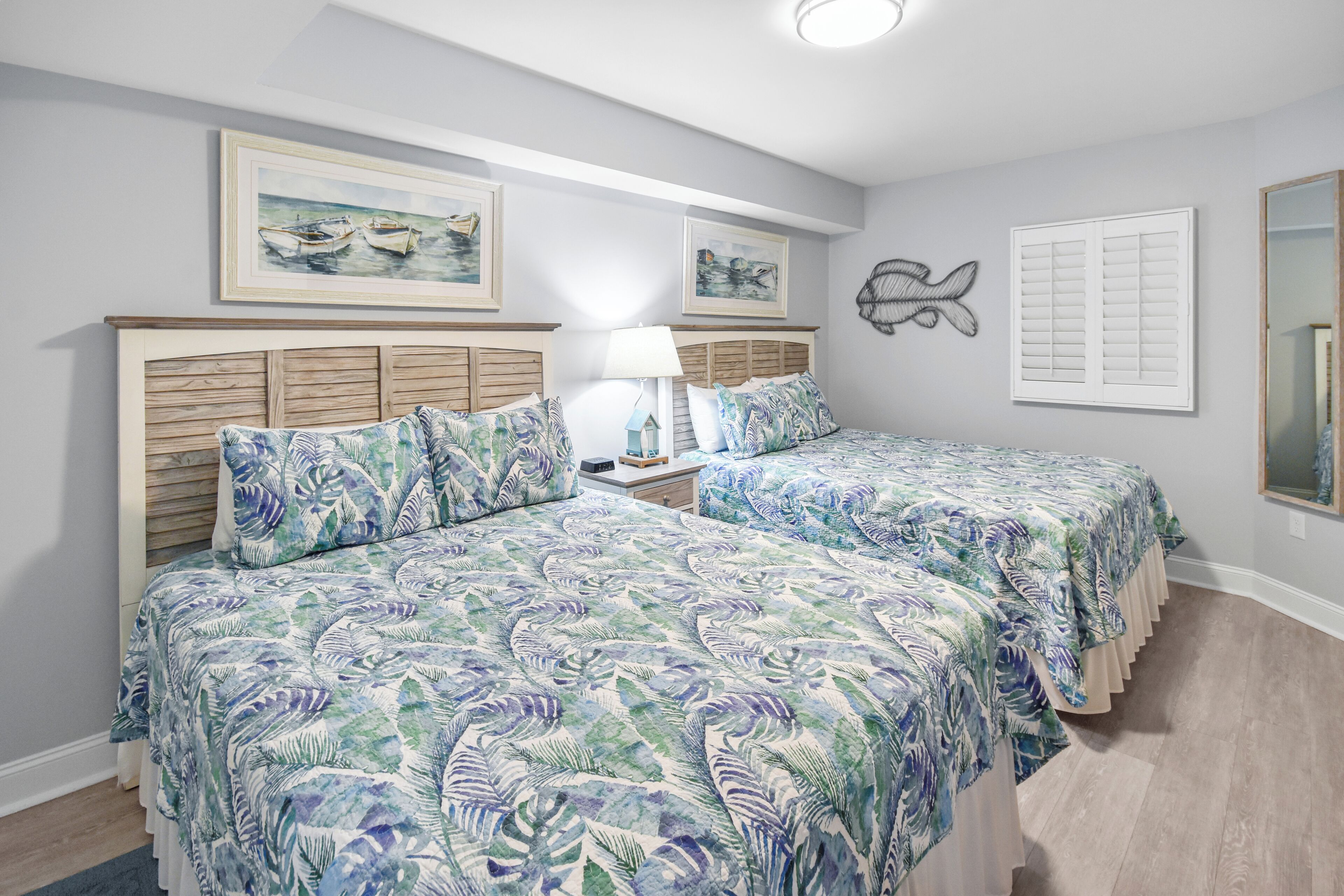 A bedroom with two beds, a nightstand, a lamp, and artwork on the walls.