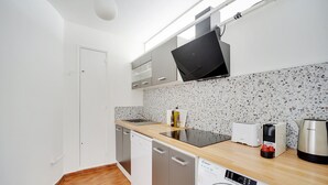 Een kleine keuken met een vaatwasser, wasmachine en een flatscreen televisie boven de aanrecht.