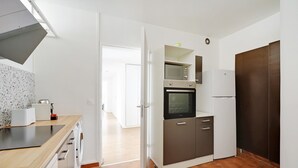 Een functionele keuken met een magnetron, oven en koelkast, een houten aanrechtblad en een deur naar een andere kamer.