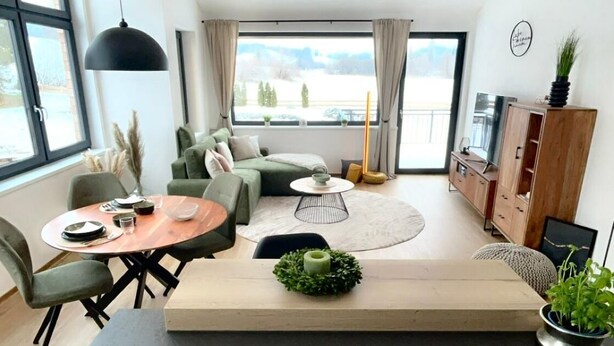 A modern living room with a sofa, a dining table, and a kitchen area with a stove. - Moosmühle Weitnau - Loft Sonneck Arrive and feel good! (Weitnau)