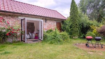 A brick house with a red-tiled roof, a patio with outdoor exercise equipment, and a barbecue grill.