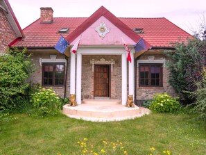 A two-story house with a red-tiled roof, a central wooden door, and a small porch with white columns. - Atmospheric Holiday Home With a Swimming Pool (gmina Dobra)