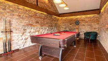 A billiards room with a pool table, a dartboard, and a green armchair.
