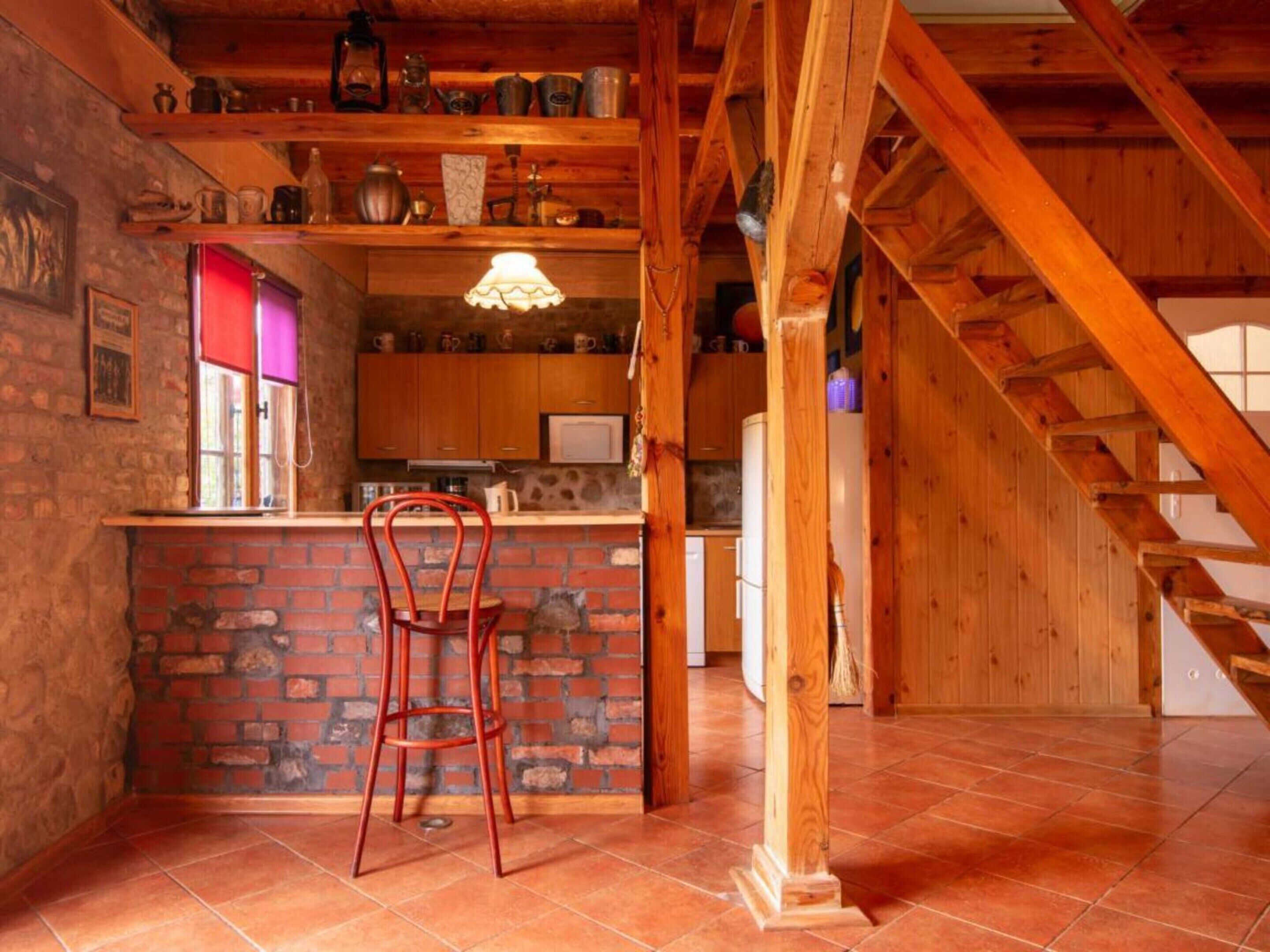 A rustic kitchen with a brick wall, wooden beams, a bar area, and a red chair.