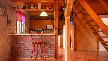 A rustic kitchen with a brick wall, wooden beams, a bar area, and a red chair.