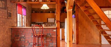 Una cocina rústica con pared de ladrillo, vigas de madera, zona de bar y una silla roja.