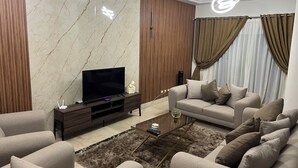 Un salón moderno con un televisor de pantalla plana, mueble de madera oscura, sofá color beige y una alfombra mullida.