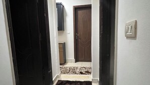 Un pasillo estrecho con un tapete oscuro, una puerta de madera y un interruptor de luz en la pared.