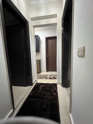 A narrow hallway with a dark rug, a wooden door, and a light switch on the wall. - Terrific 5-bedroom villa with AC in New Cairo City in compound (New Cairo City)