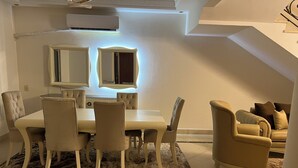 Un comedor con una mesa y sillas blancas, un tapete estampado y un sofá con cojines.