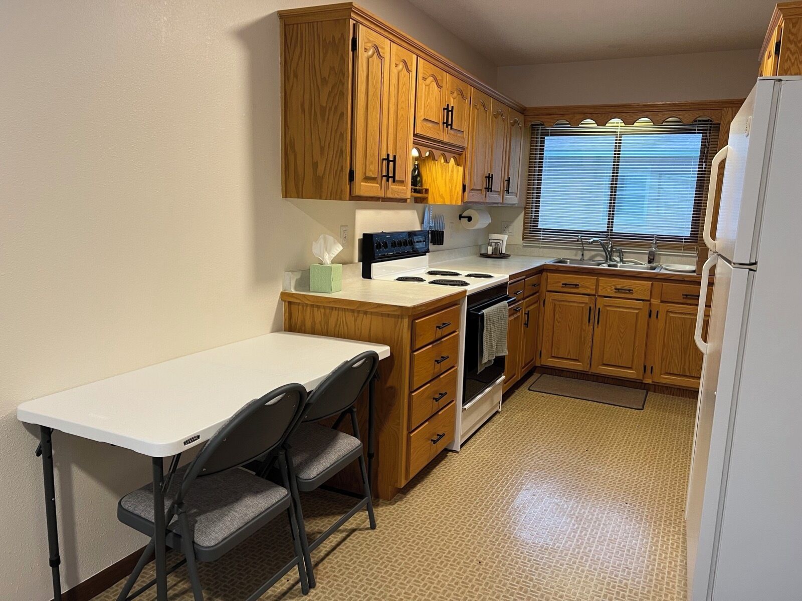 A compact kitchen with wooden cabinets, a stove, a sink, and a small dining table with chairs.