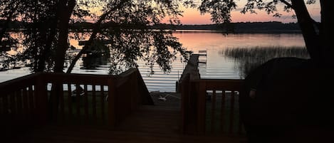 Una terraza de madera que conduce a un lago tranquilo, con árboles enmarcando la vista.