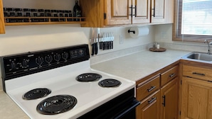 A kitchen with wooden cabinets, a white stove, and a window with blinds. - Clean and Cozy Lakefront cabin on Ida Lake (Monticello)