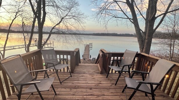 A wooden deck with chairs and tables, overlooking a body of water. - Clean and Cozy Lakefront cabin on Ida Lake (Monticello)