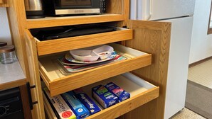 A kitchen with a microwave, a kettle, and a refrigerator. There are wooden cabinets with drawers containing kitchenware and storage boxes. - Clean and Cozy Lakefront cabin on Ida Lake (Monticello)