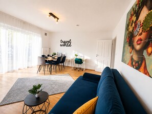 Un salon moderne avec un canapé bleu, un coin repas comprenant une table et des chaises, et un grand tableau accroché au mur.