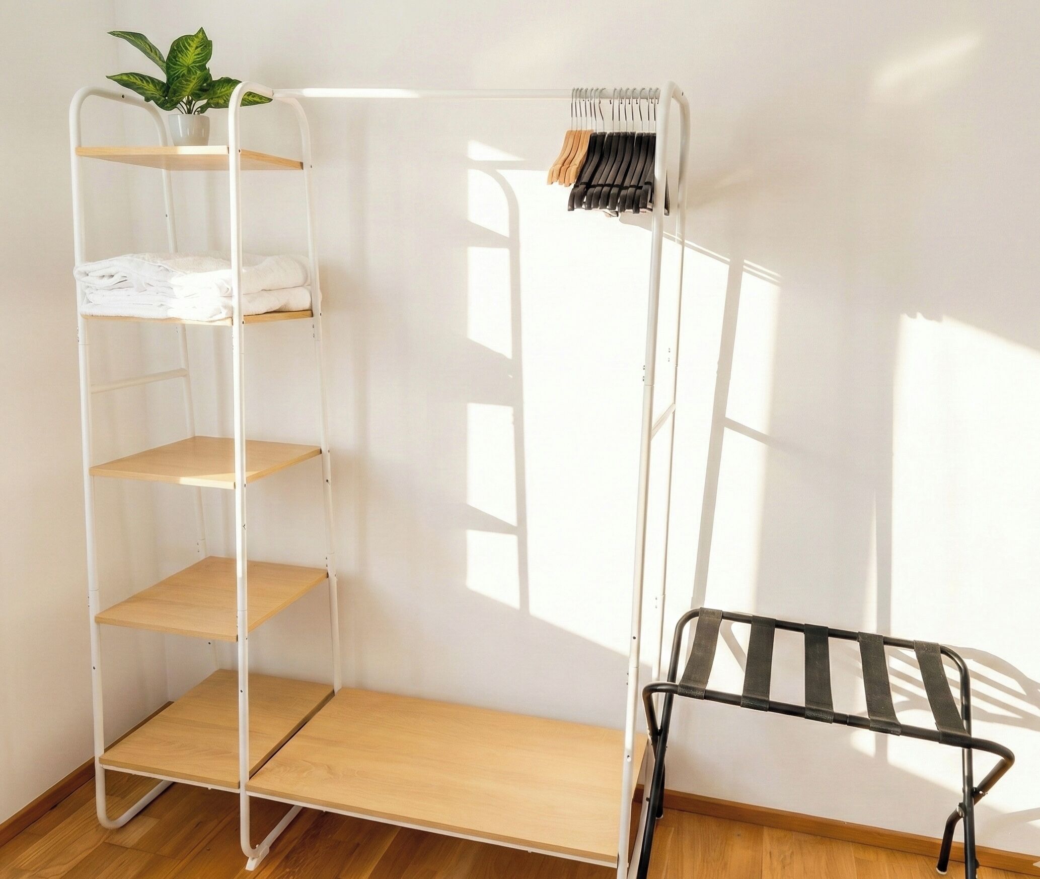Ein Zimmer mit einem weißen Metallregal, einem schwarzen Gestell und einem Blumentopf.