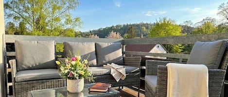Un área de estar exterior con muebles de mimbre, cojines, una mesa de vidrio y una planta en maceta.