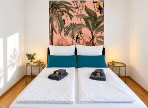 Un lit double avec du linge de lit blanc, des coussins turquoise et deux tables de chevet avec des lampes.