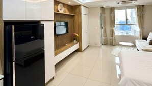 A modern hotel room with a kitchenette, a flat-screen TV, a bed, a small table, and a window with curtains. - Sunrise High Floor Pool Ben Thanh Gym (Ho Chi Minh City)