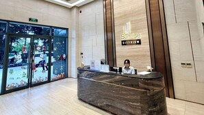 A modern hotel reception area with a marble reception desk, a receptionist, and a large glass door entrance. - Sunrise High Floor Pool Ben Thanh Gym (Ho Chi Minh City)