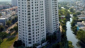 A high-rise building with multiple floors, a river in the foreground, and a cityscape in the background. - Sunrise High Floor Pool Ben Thanh Gym (Ho Chi Minh City)