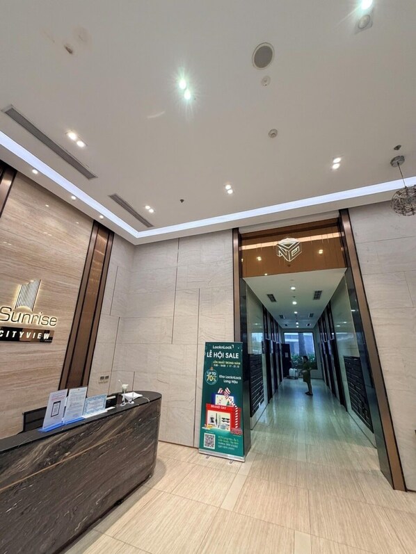 Um saguão moderno de hotel com balcão de recepção, um aviso de promoção e vista para o corredor do hotel.