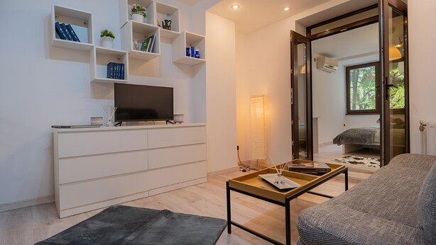 Ett modernt vardagsrum med en platt-TV, vita hyllor med dekorativa föremål, en soffa och ett soffbord.