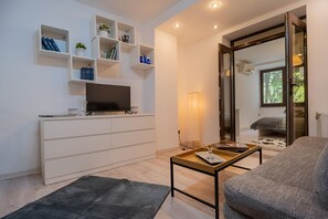 Ein modernes Wohnzimmer mit Flachbildfernseher, weißen Regalen mit Dekoration, einer Couch und einem Couchtisch.