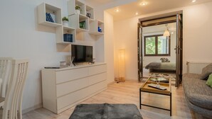 Ett modernt vardagsrum med en platt-TV, vita hyllor, ett soffbord och en soffa.