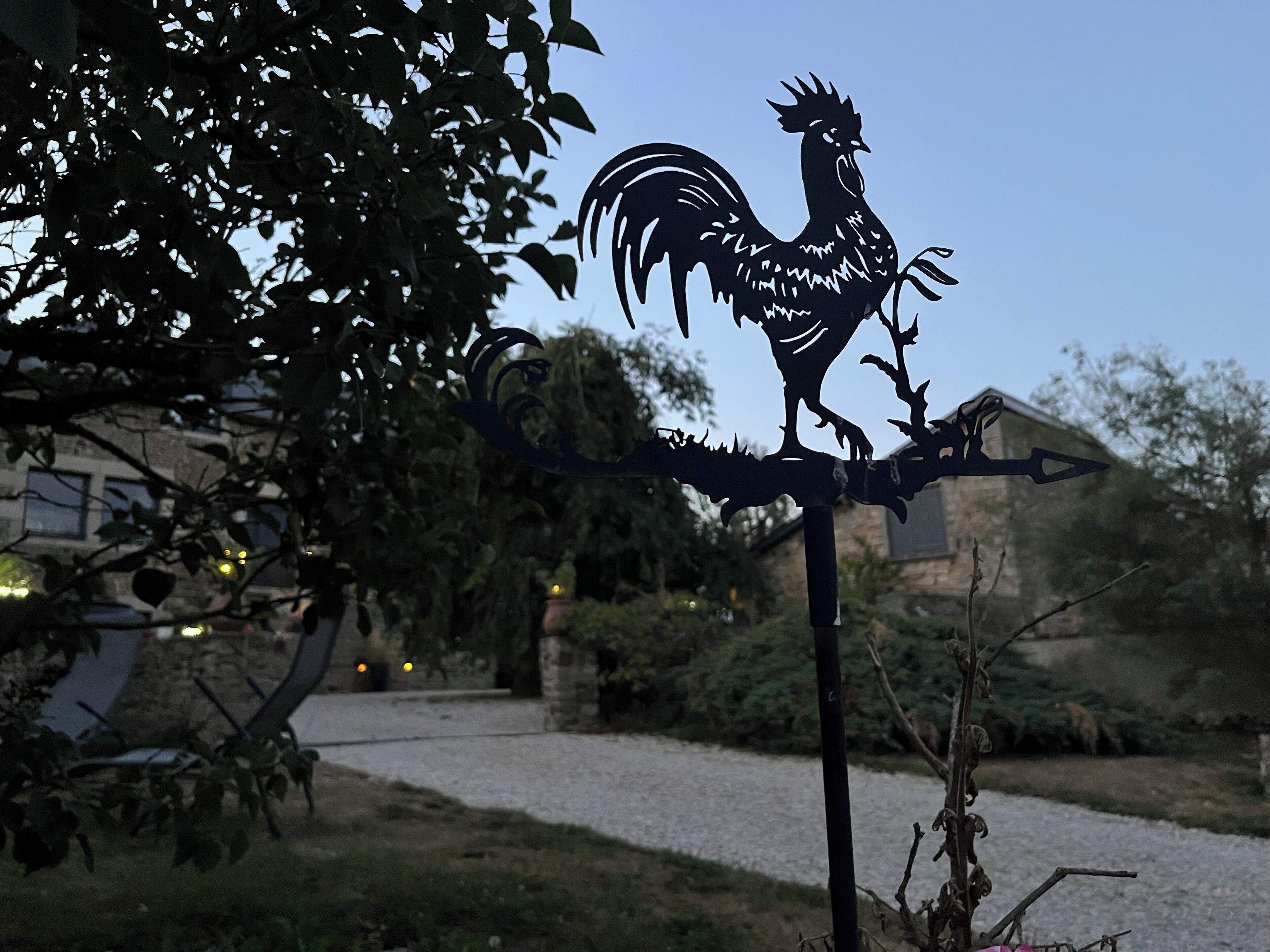 Ein Schild in Form eines Metallroosters mit einem Pfeil, vor einer Fassade aus Stein und Grünpflanzen.