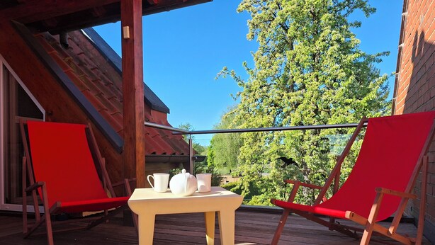 Een houten terras met twee rode stoelen en een tafel met witte bekers en een theepot.