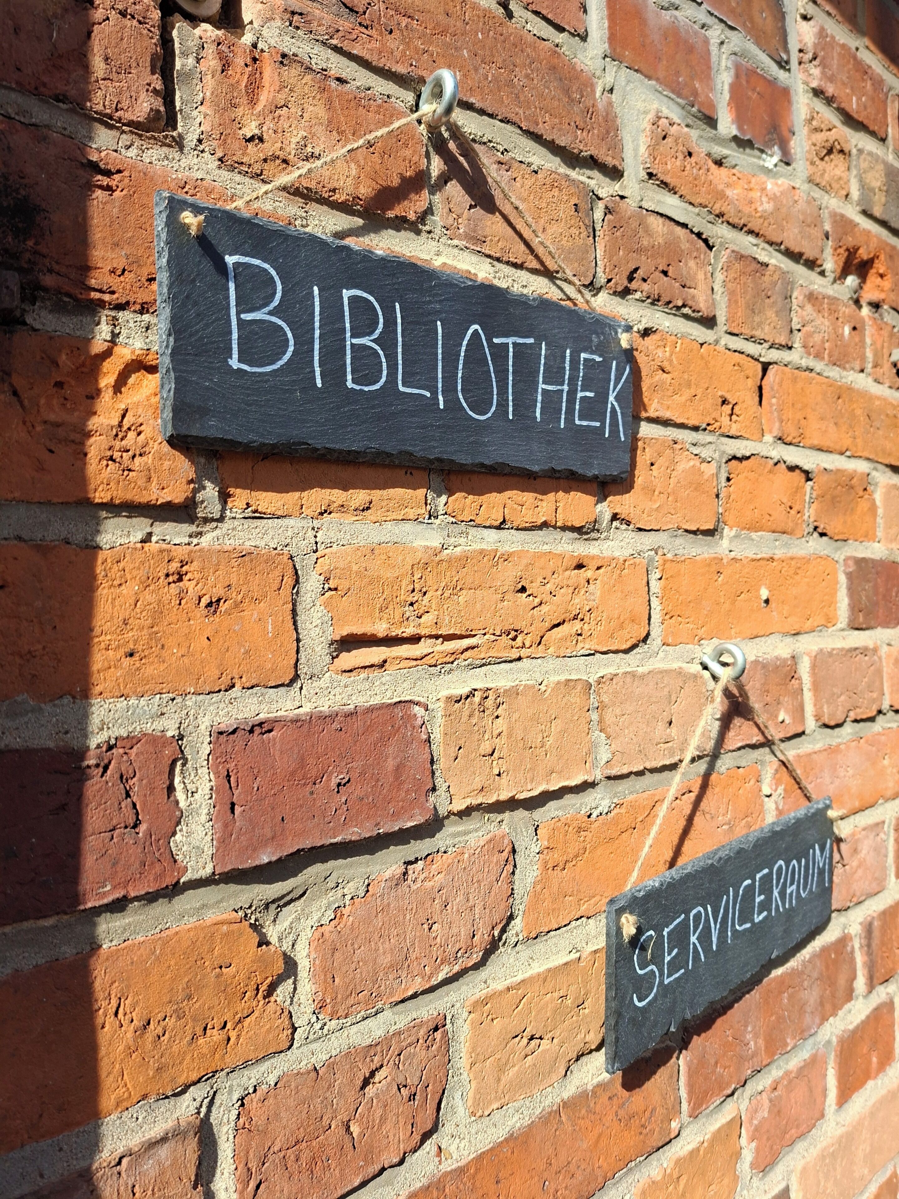 Un mur de briques sur lequel sont apposées deux enseignes : « BIBLIOTHEK » et « SERVICERAM ».
