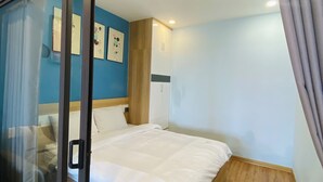 Een slaapkamer met een bed, houten vloeren, een blauwe accentmuur en een schuifglazen deur.