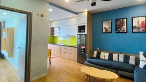 Een moderne woonkamer met een bank, salontafel en plafondventilator. Achtergrond toont een keuken met een koelkast en een eettafel.