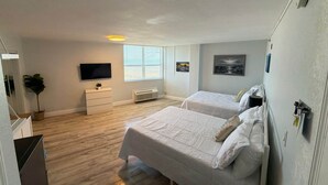Een hotelkamer met twee bedden, een televisie, een kaptafel, een plant en kunstwerken aan de muur.