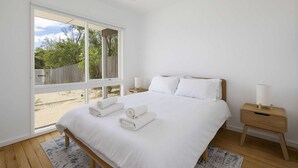 A bedroom with a large window, a bed with white linens, two bedside tables with lamps, and a view of greenery outside. - Peaceful 2-bed Apartment in Coastal Mccrae (Melbourne)