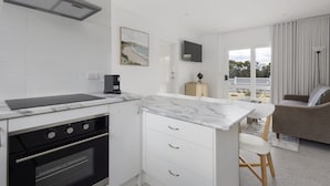 A modern kitchen with white cabinetry, a built-in oven, a countertop with a coffee maker, and a view of the outdoors through large windows. - Peaceful 2-bed Apartment in Coastal Mccrae (Melbourne)