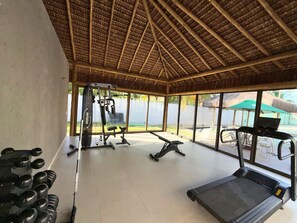 Ein Fitnessraum mit Trainingsgeräten, Laufband und großen Fenstern mit Blick auf einen Garten.