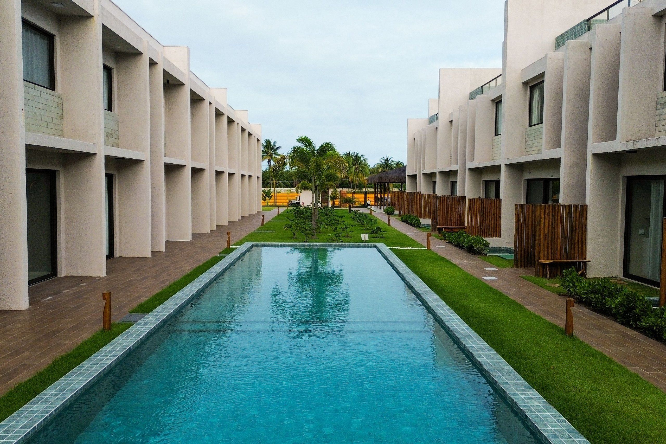 A modern hotel with a central swimming pool, surrounded by neatly arranged rooms and a well-maintained lawn.