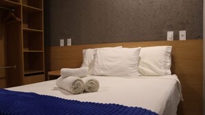 Una camera d'albergo con un letto rifatto, una coperta blu e una testiera in legno.