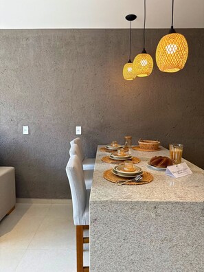 A modern dining area with a marble countertop, woven placemats, and a candle centerpiece.