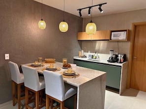 A modern kitchen with a dining area, featuring a granite countertop, wooden chairs, and pendant lighting.